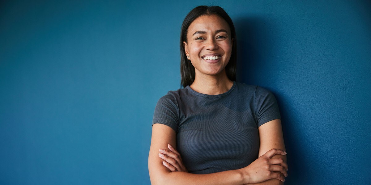 woman with crossed arms smiling in front of blue background